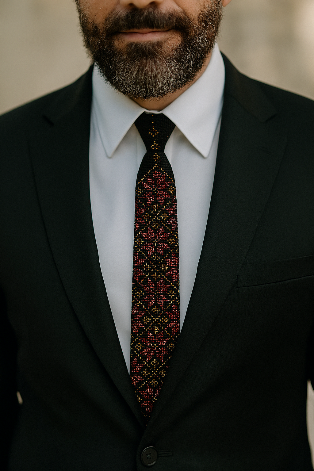 Man wearing a black suit with a Rumman tatreez tie with pomegranate-inspired embroidery.